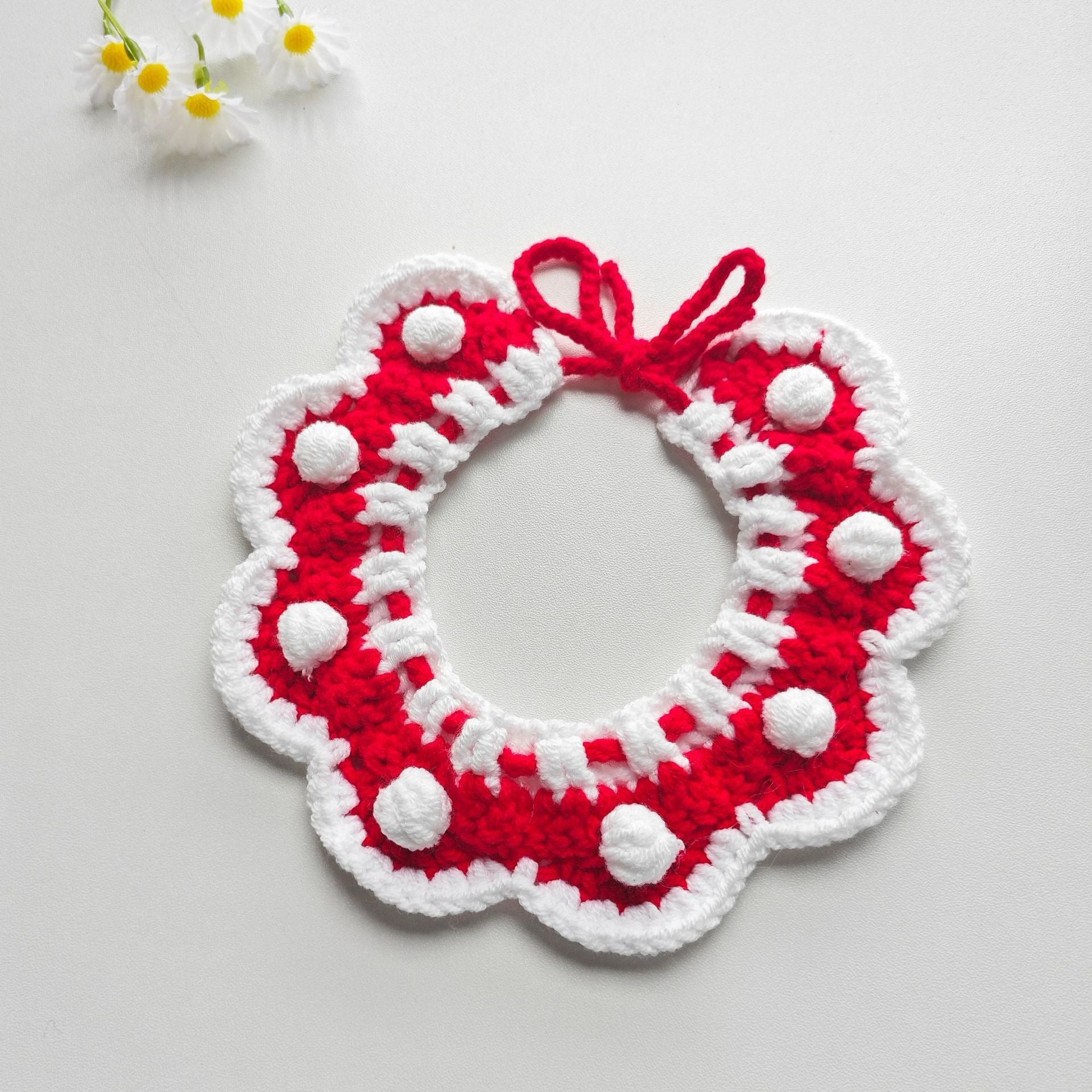 Red and white crochet pet collar with a large 3D flower and small pom-poms, designed for cats and small dogs’ festive wear