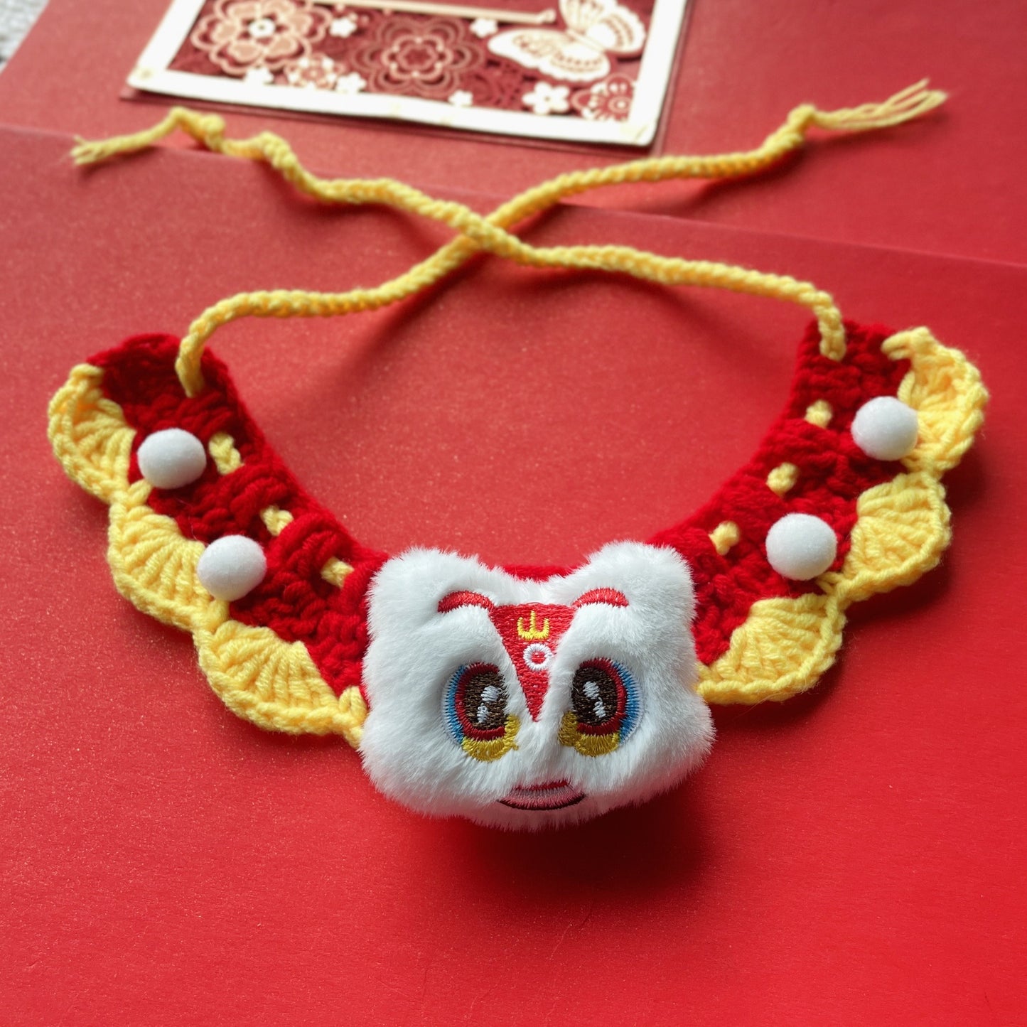 Red and white crochet pet collar with 3D flowers, pom-poms, and a bell, displayed flat to show detailed craftsmanship.