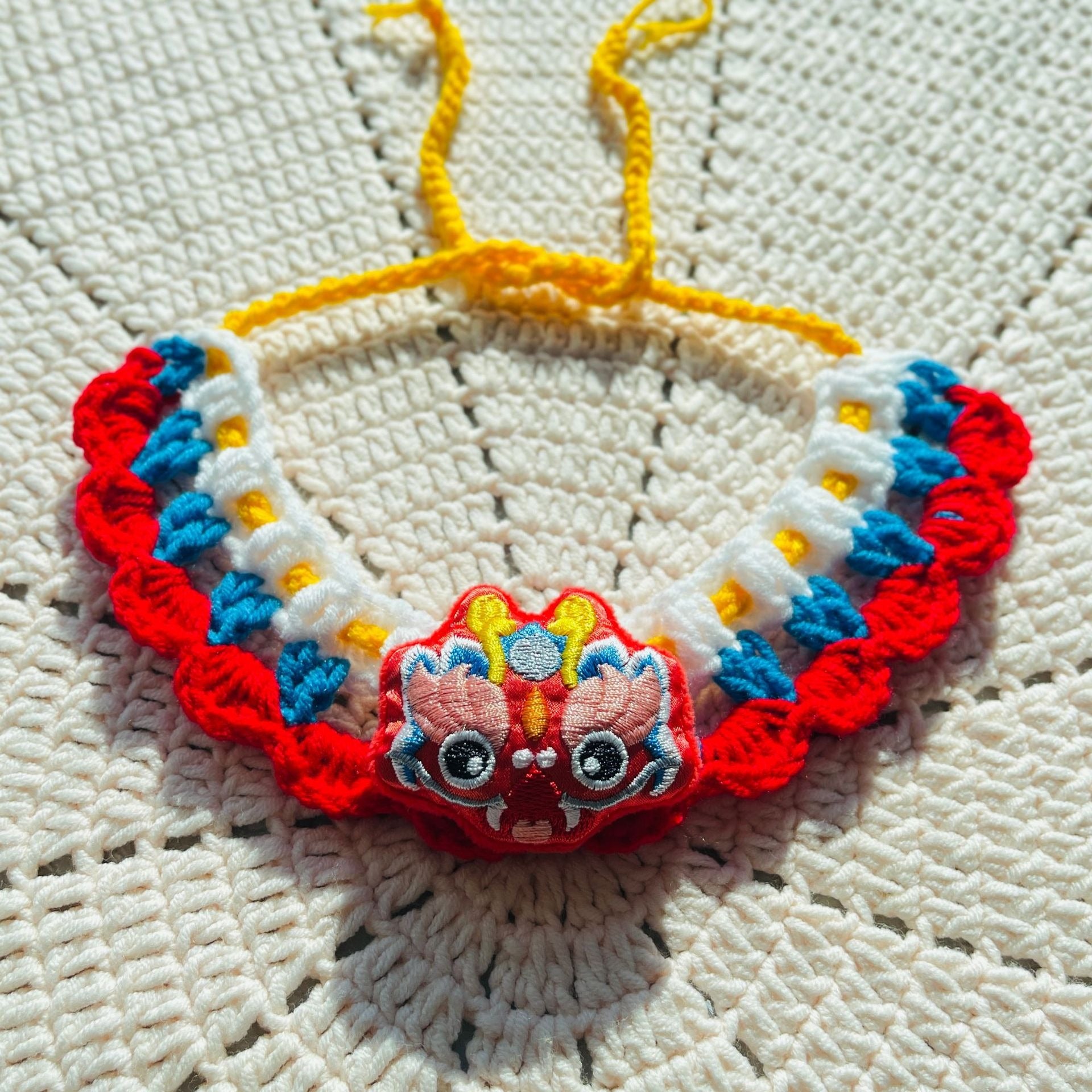 Colorful crochet pet collar with red, blue, and white details, 3D flowers, and a bell, showcasing the handwoven texture
