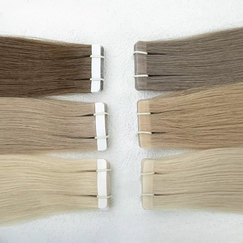 Various shades of tape-in hair extensions laid out, including light blonde and brown, for color selection.