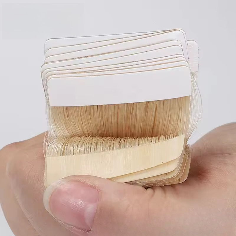 Close-up of stacked tape-in hair extensions, held by a hand to show the thickness and adhesive tape.
